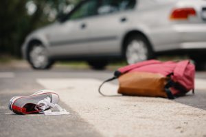 A backpack and sneaker lay on the ground with a car nearby implying a pedestrian accident occurred.