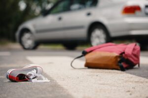 Savannah Pedestrian Accident Lawyers | John Foy & Associates A backpack and sneaker lay on the ground with a car nearby implying a pedestrian accident occurred.