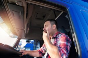 A truck driver yawns tiredly at the wheel.