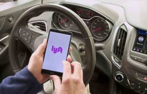Mableton Rideshare Accident Lawyers | John Foy & Associates A person sits in the driver’s seat holding a phone with the Lyft app opening.