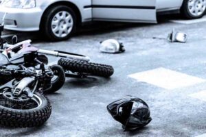Warner Robins Motorcycle Accident Lawyers | Support Available 24/7 A crashed motorcycle lies near a damaged car. A helmet and broken side-view mirror lie on the ground as well.