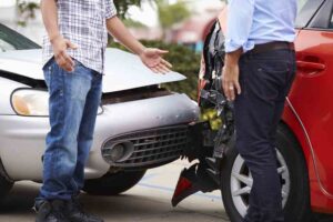 Two people involved in a car accident talk near their damaged cars.