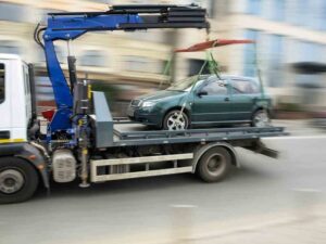 Mableton Tow Truck Accident Lawyers | Support 24/7 | Hablamos Español A tow truck carrying a car drives fast out of an underground garage into the street.