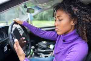 A woman is looking at her phone while driving on the road.