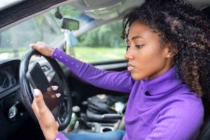 Warner Robins Texting While Driving Accident Lawyers | Free Case Reviews A woman is looking at her phone while driving on the road.