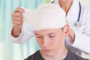 A young man gets his head bandaged by a doctor.
