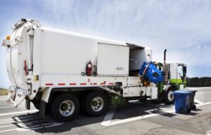 Athens Garbage Truck Accident Lawyer | Free No-Risk Consultations A garbage truck uses its hydraulic arm to collect trash from a bin on the sidewalk.