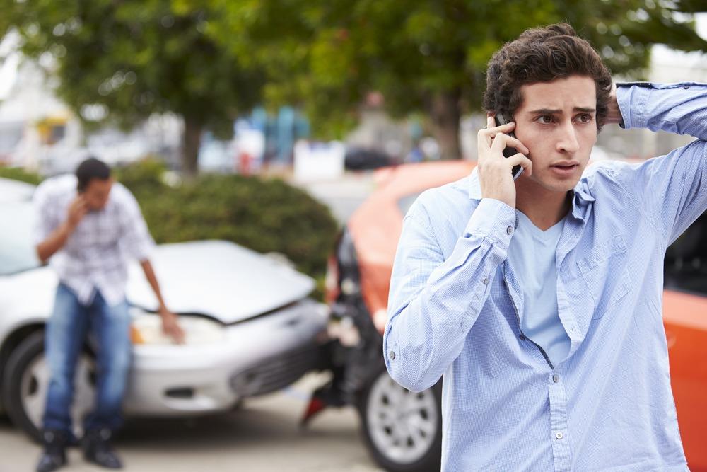 A young driver talks on the phone at the scene of a car crash.