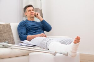 Ellenwood Personal Injury Lawyers | John Foy & Associates injured man with crutches on couch talking to lawyer on phone