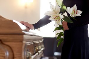 A woman holds flowers while touching a coffin.
