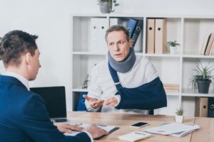 Riverdale Workers’ Compensation Lawyer | Free Consultations An injured man talks to a lawyer at his desk.