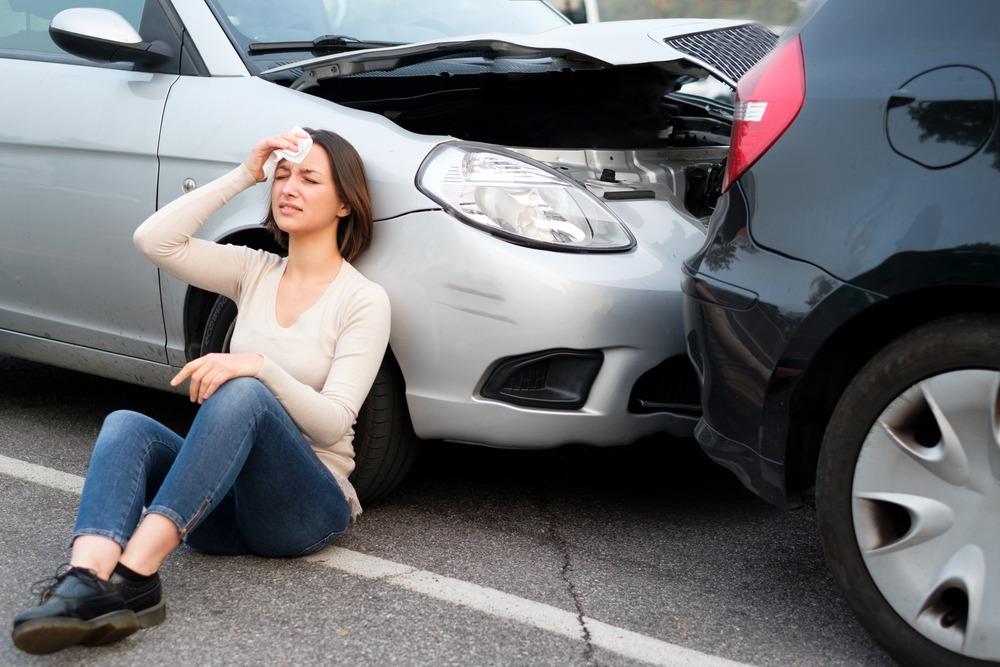 An injured woman sits next to her car after a rear-end accident.
