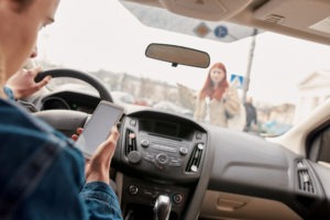 man texting while driving as a pedestrian approaches