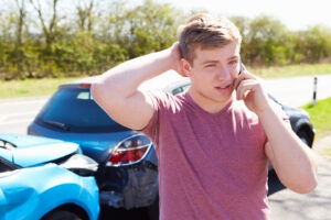 a teenage boy making a phone call at an accident scene after rear-ending someone