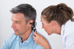 a female doctor examining a male patient’s ear using an otoscope