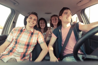 Four teens smile as they drive in a car because they know about the 100 deadliest days of summer and understand teen driving risks.