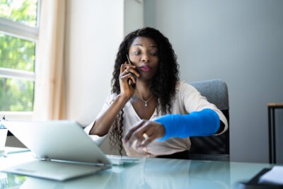 injured woman with her arm in a cast asking someone over the phone about what to do if workers’ comp issues are delaying your medical treatment.