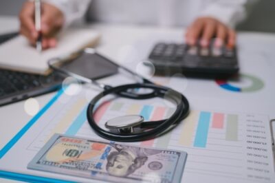 A stack of dollar bills and a stethoscope lie next to medical bills on a table while an injured worker sits in the background researching what happens to medical bills if workers’ compensation is denied.